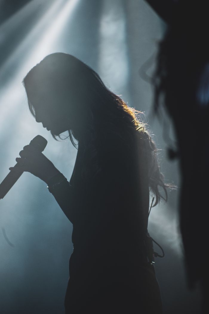 Silhouette of a female singer holding a microphone on stage, captured in a dramatic light.