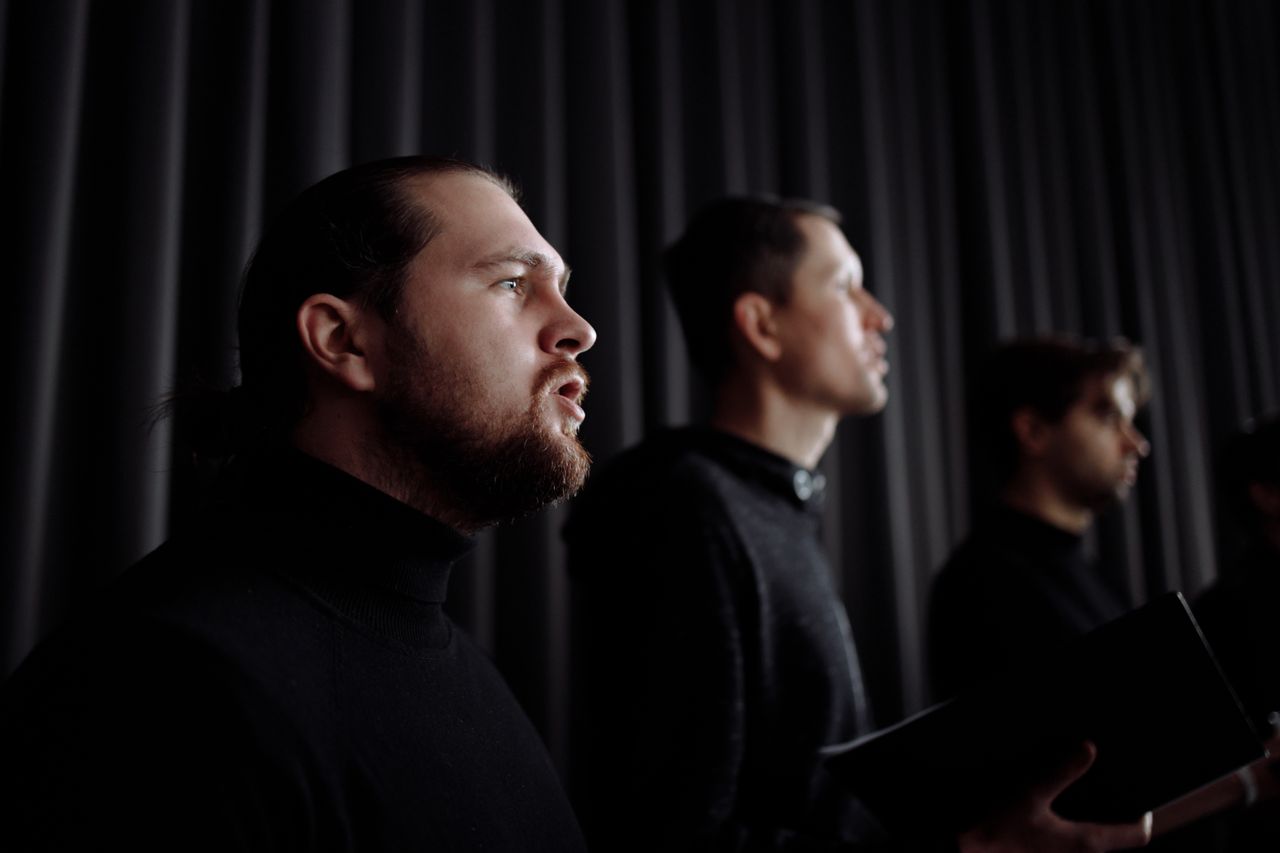 A group of male singers performing passionately indoors, dressed in dark attire, creating an elegant atmosphere.